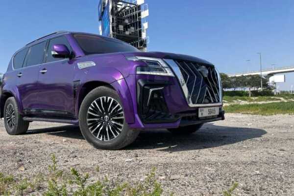 A striking purple Nissan SUV parked on rugged ground, showcasing its bold design and stylish black rims under clear blue skies.