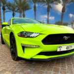 A vibrant lime green Ford Mustang EcoBoost parked in a palm-lined area, showcasing its sleek design and distinctive branding.