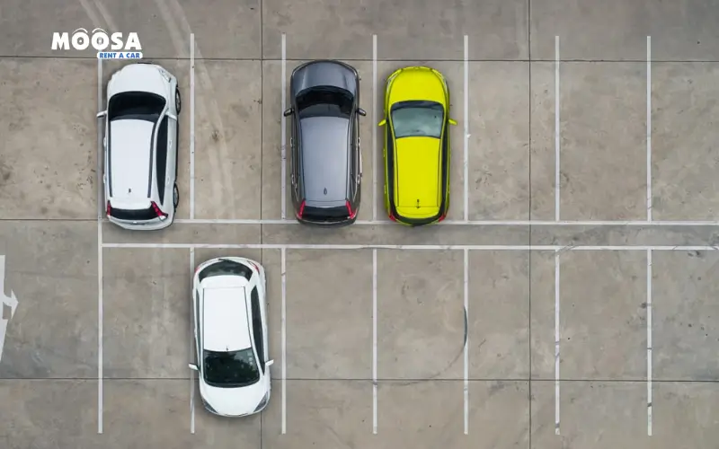 Aerial view of umm al qawain zoo parking in which four parked cars: two white, one gray, and one bright yellow, in a mostly empty parking lot with clear lines.