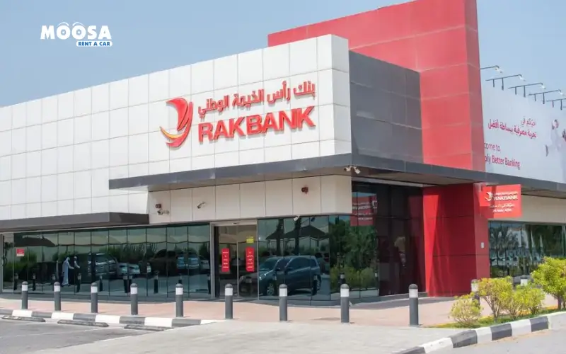 Exterior view of a modern RAKBANK branch with a glass facade, featuring the bank's logo and signage in Arabic and English.