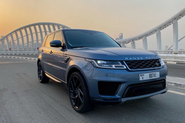 A sleek blue Range Rover parked on a bridge with a modern architectural design, under a golden sunset sky.